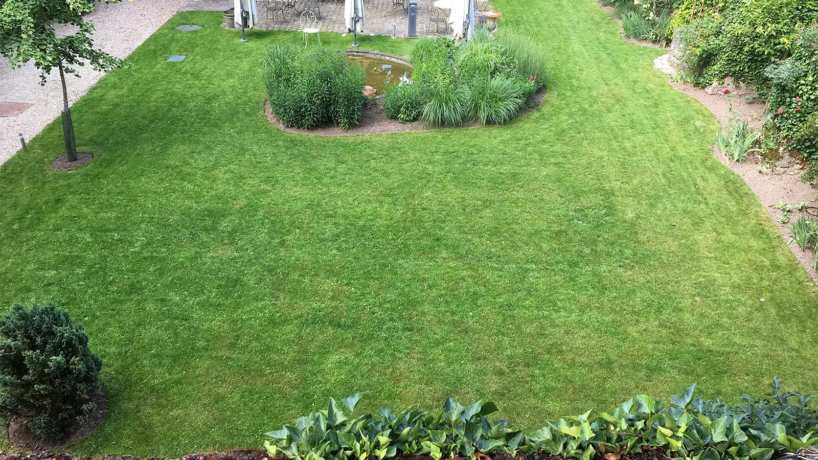 Jardin paysager avec pelouse, bassin et massifs autour d’une bâtisse en pierre